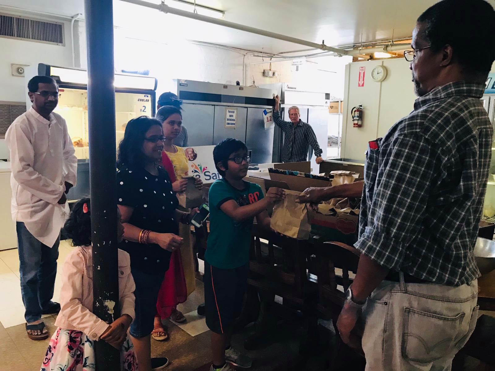 A young I Love Sai volunteer hands a packed meal to a partner organization's staff member